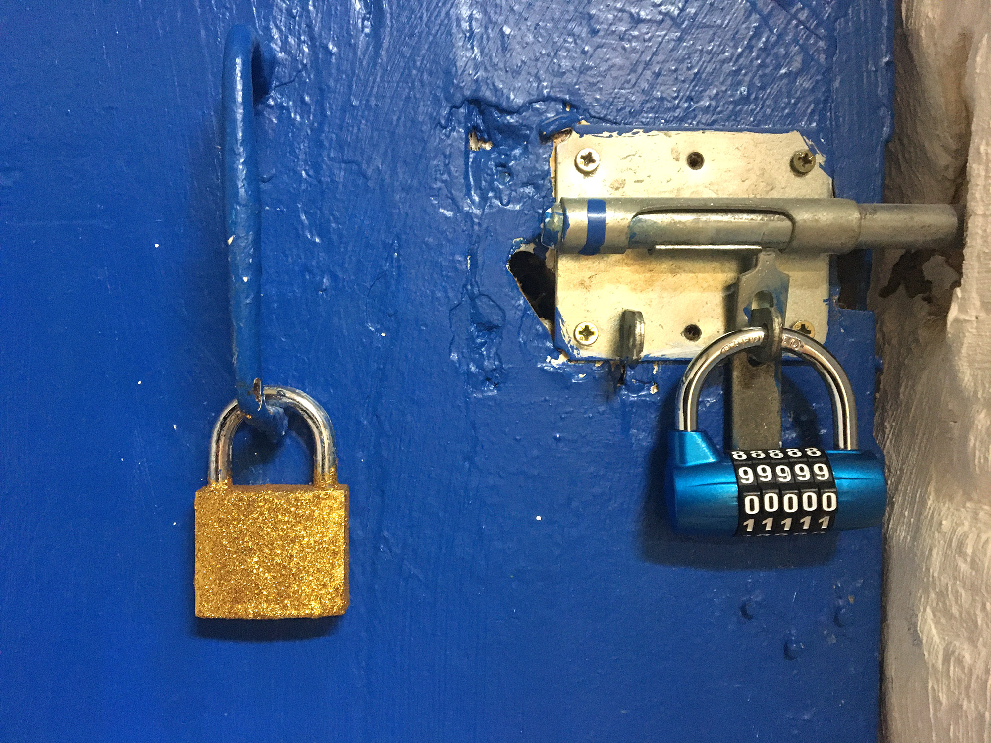 Un cadenas est accroché sur uen porte bleue. Il est recouvert de paillettes dorées. On voit qu'il est posé à côté d'un cadenas à code et qu'en réalité il ne cadenasse rien.